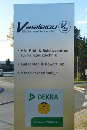 Pylon-Stele am Eingang der Prüfstelle in Lahnau mit Vasileiou-Logo und DEKRA-Prüfstützpunkt-Schild